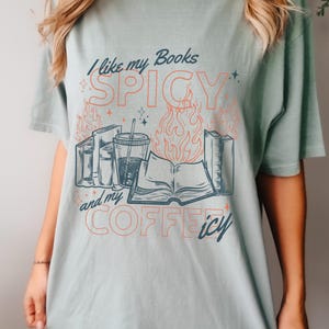 May include: A light green t-shirt with the text "I like my Books SPICY and my COFFEE icy." The graphic includes illustrations of books, flames, and a beverage with a straw. The shirt is a casual style.