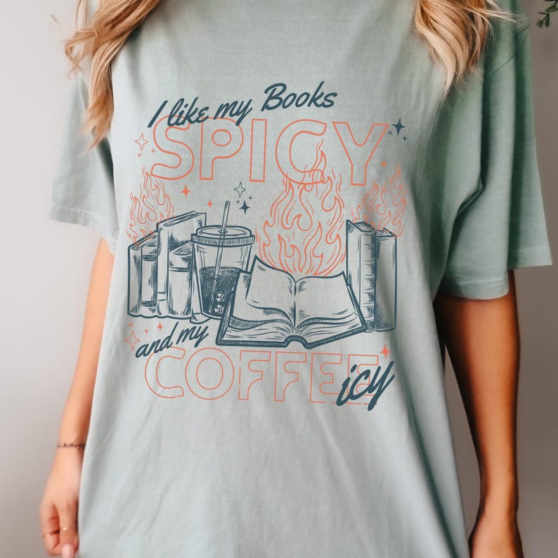 May include: A light green t-shirt with the text "I like my Books SPICY and my COFFEE icy." The graphic includes illustrations of books, flames, and a beverage with a straw. The shirt is a casual style.