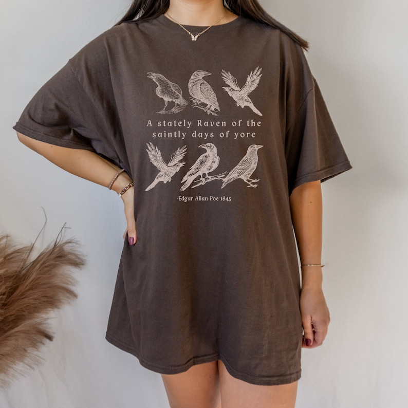 以下が含まれることがあります： カラスのグラフィックプリントと「A stately Raven of the saintly days of yore - Edgar Allan Poe 1845」というテキストがプリントされた、茶色のオーバーサイズTシャツです。