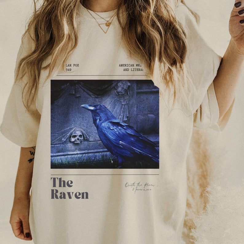 May include: A white t-shirt with a graphic of a raven perched on a tombstone. The text "The Raven" is printed below the image, along with the quote "Once the raven I evermore."