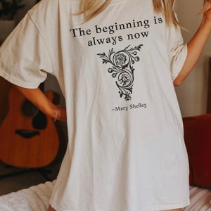 May include: White oversized t-shirt with black text that reads "The beginning is always now" and a floral design. The text "~Mary Shelley" is below the design.