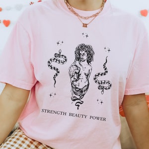 May include: Pink t-shirt with a black and white illustration of a woman with snakes and the text "STRENGTH BEAUTY POWER".