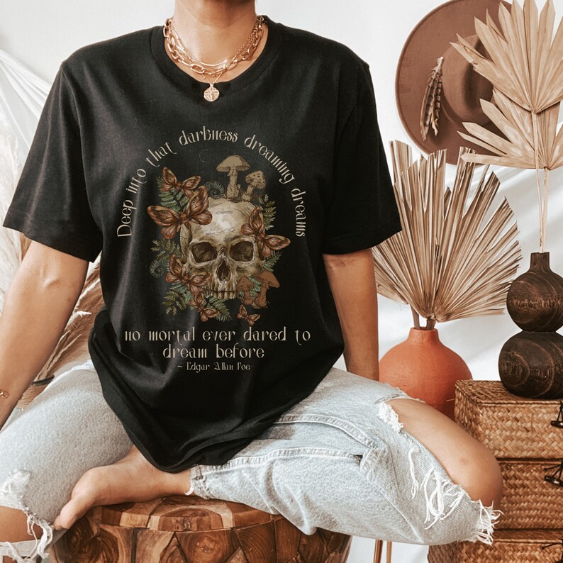 May include: Black t-shirt featuring a skull and floral design. The text reads "Deep into that darkness dreaming dreams no mortal ever dared to dream before - Edgar Allan Poe".