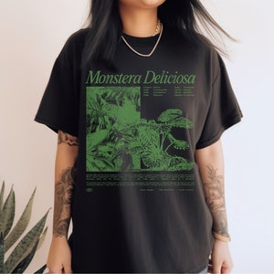 May include: Black t-shirt with a green print of a Monstera Deliciosa plant. The print includes the scientific classification of the plant: Kingdom: Plantae, Order: Alismatales, Class:  Liliopsida, Family: Araceae, Genus: Monstera, Species: Deliciosa.