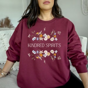 May include: Burgundy sweatshirt with a floral design and the text "KINDRED SPIRITS" printed on the front.