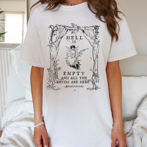May include: White t-shirt with a black and white graphic print of a fairy sitting on a thorny bush. The graphic includes the text "Hell is empty and all the devils are here -Shakespeare".