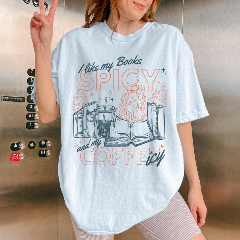 May include: Light blue t-shirt with the text "I like my Books SPICY and my COFFEE icy." The graphic features books, a coffee cup, and flames. The shirt is a casual, oversized fit.