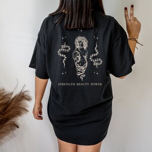 May include: Black oversized t-shirt with a graphic print of a woman with snakes and the text "STRENGTH BEAUTY POWER".