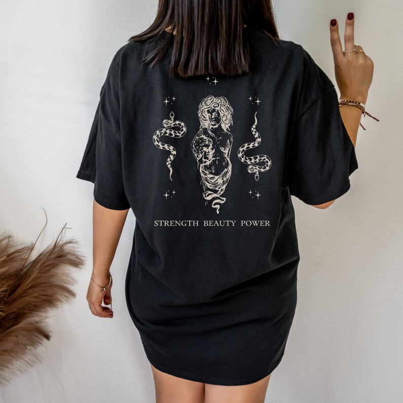 May include: Black oversized t-shirt with a graphic print of a woman with snakes and the text "STRENGTH BEAUTY POWER".