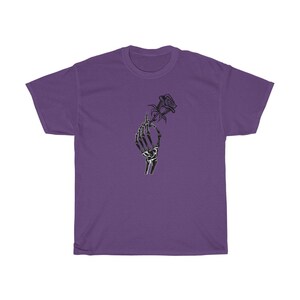 K&ouml;nnte beinhalten: Ein lila T-Shirt mit einer schwarz-wei&szlig;en Grafik einer Skeletthand, die eine Rose h&auml;lt.