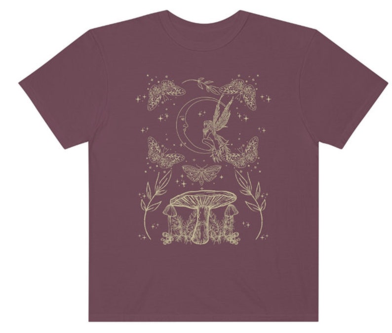 Pu&ograve; includere: Una t-shirt color granata con un contorno bianco di una fata, una luna crescente, falene e funghi. Il design &egrave; in stile fantasioso.