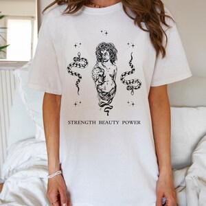 May include: White t-shirt with a black and white illustration of a woman with snakes and the text "STRENGTH BEAUTY POWER".