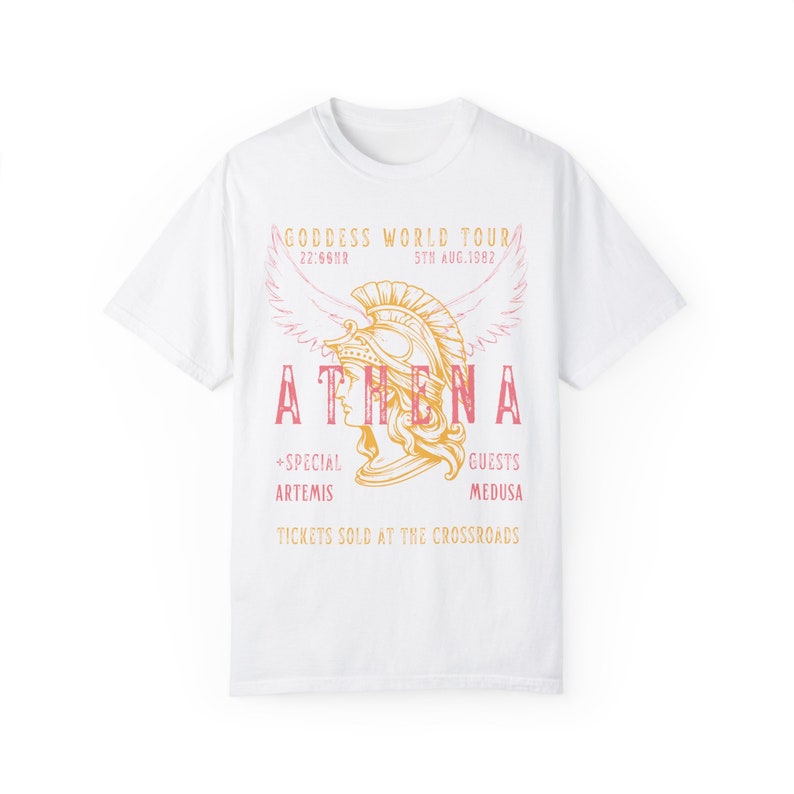 Puede incluir: Camiseta blanca con un dise&ntilde;o gr&aacute;fico de una mujer con un casco con alas. El texto dice "GODDESS WORLD TOUR", "ATHENA", "+SPECIAL ARTEMIS", "GUESTS MEDUSA", y "TICKETS SOLD AT THE CROSSROADS".