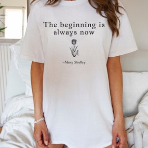 May include: White t-shirt with the text "The beginning is always now" and a small flower graphic. The quote is attributed to "Mary Shelley".