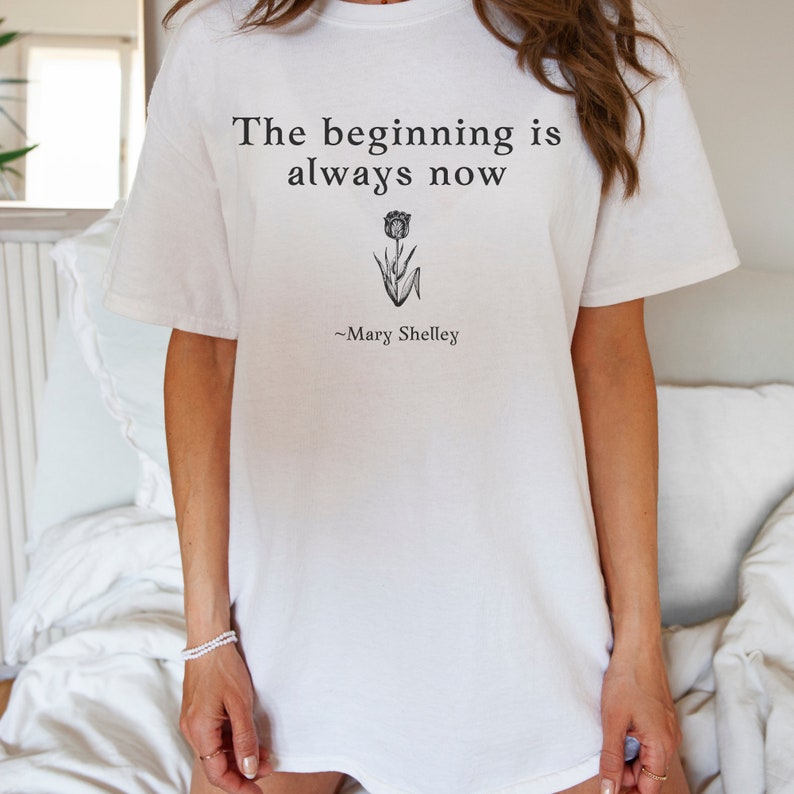 May include: White t-shirt with the text "The beginning is always now" and a small flower graphic. The quote is attributed to "Mary Shelley".