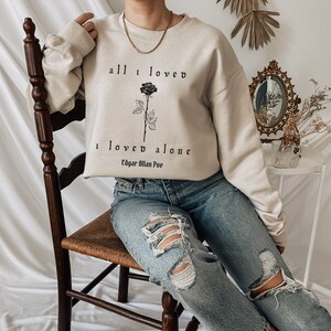 May include: A beige sweatshirt with a black rose and the text "all I loved I loved alone Edgar Allan Poe" printed on the front.