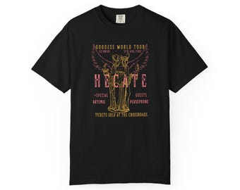 May include: A black short-sleeve t-shirt featuring a graphic print with the text GODDESS WORLD TOUR, HECATE, and TICKETS SOLD AT THE CROSSROADS. The design includes a central illustration of a winged figure and yellow and pink accents.