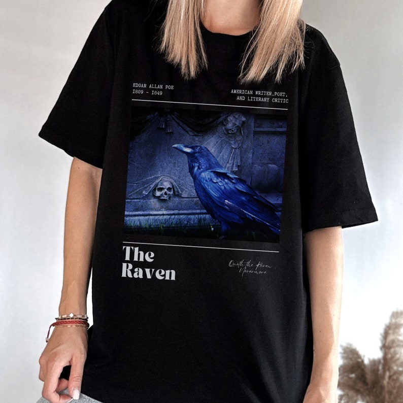 May include: Black t-shirt with a graphic print of a raven perched on a tombstone. The text "The Raven" is printed below the image. The text "Edgar Allan Poe 1809 - 1849 American Writer, Poet, and Literary Critic" is printed above the image.