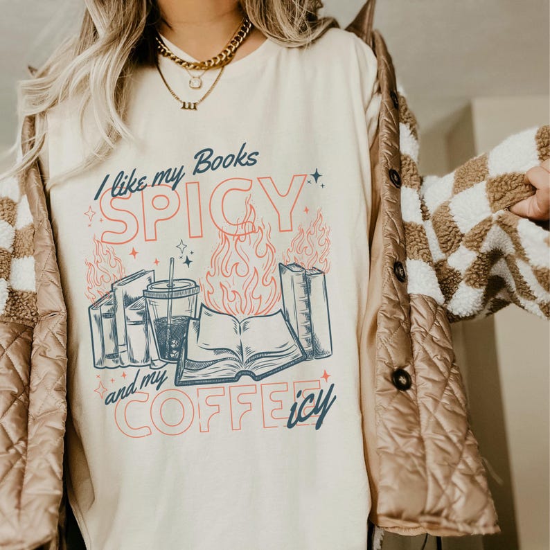 May include: Cream-colored t-shirt with the text "I like my Books SPICY and my COFFEE icy" in blue and red. The graphic includes books, flames, and a coffee cup. The shirt is part of a casual wear collection.