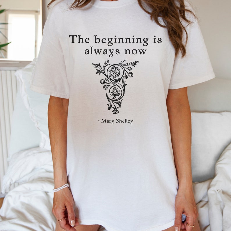 May include: White t-shirt with a black graphic print that reads "The beginning is always now" and "~Mary Shelley".