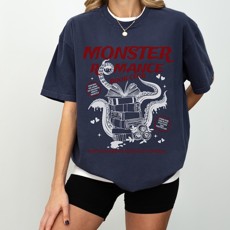 Pu&ograve; includere: T-shirt blu navy con la scritta rossa "MONSTER ROMANCE BOOK CLUB". Il design presenta una pila di libri con un polpo e cuori. La maglietta ha anche le frasi "ONE BED, SOLOS, NO REGRETS, MEETS NIGHTLY" e "COME FOR THE TENTACLES".