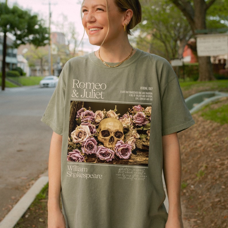 May include: Green t-shirt with a graphic print of a skull surrounded by pink roses. The text "Romeo & Juliet" and "William Shakespeare" are printed on the shirt.