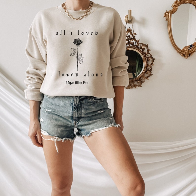 May include: A beige sweatshirt with a black rose and the text "all I loved I loved alone Edgar Allan Poe" printed on the front.