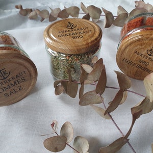 May include: Three glass jars with wooden lids and labels. The labels read "Ankerkraut Pommes Salz", "Ankerkraut BBQ", and "Ankerkraut BBQ Sizzle Brother".
