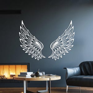 Könnte beinhalten: Weiße Engelsflügel-Wandkunst. Die Flügel sind an einer dunkelgrauen Wand in einem modernen Wohnzimmer dargestellt. Der Raum verfügt über einen Kamin, einen schwarzen Ledersessel und einen Holztisch.