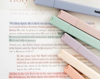 May include: A collection of pastel-colored highlighters, including light blue, pink, green, purple, and peach, are arranged diagonally across an open book. The highlighters are highlighting text on the page. The word "rese" is visible on one highlighter.