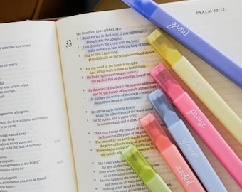May include: A collection of colorful highlighters with the words "grow", "praise", "flourish", "rooted", and "planted" written on them, resting on an open book. The book displays text from Psalm 33:22.