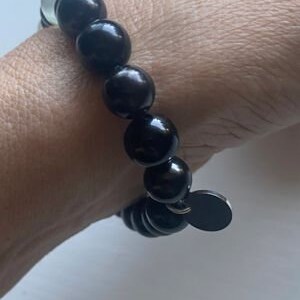 Puede incluir: Un brazalete de cuentas negras con un dije de metal negro. El brazalete está hecho de cuentas redondas negras y tiene un diseño simple y elegante.