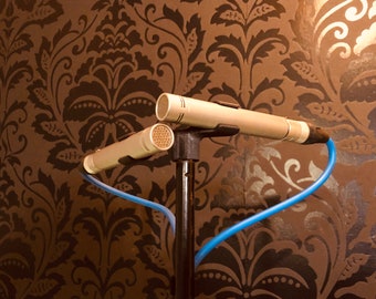 May include: Two silver microphones mounted on a black stand with blue cables. The microphones are positioned in a stereo configuration.