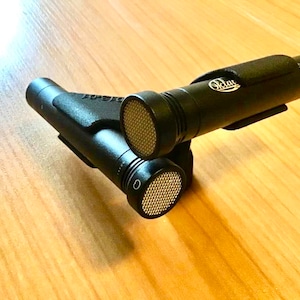 Könnte beinhalten: Zwei schwarze Mikrofone mit einem silbernen Gitter und dem Wort "Octave" auf der Seite, montiert auf einem schwarzen Ständer.