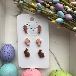 May include: A set of six clay earrings featuring Easter-themed designs. The earrings include two carrot earrings, two cross earrings, and two bunny earrings. The earrings are displayed on a white card with the text "Turquoise Clay Co."