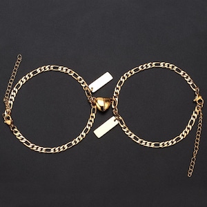 Puede incluir: Dos pulseras de cadena dorada con un dije en forma de coraz&oacute;n y dos etiquetas rectangulares. Las pulseras est&aacute;n unidas por el dije en forma de coraz&oacute;n.