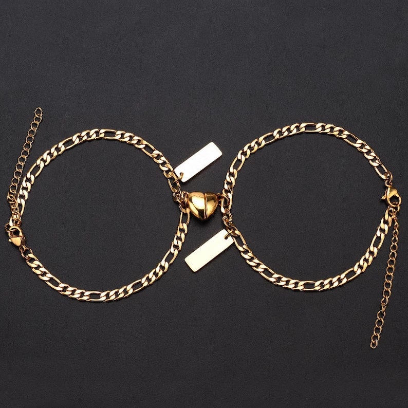 Puede incluir: Dos pulseras de cadena dorada con un dije en forma de coraz&oacute;n y dos etiquetas rectangulares. Las pulseras est&aacute;n unidas por el dije en forma de coraz&oacute;n.