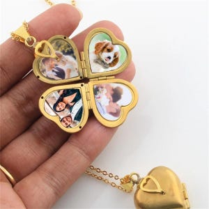 Op de afbeelding: Een goudkleurige hartvormige locket-ketting met vier hartvormige compartimenten, elk met een kleine foto. Het medaillon is open en toont de foto's. De ketting zit aan een gouden ketting.