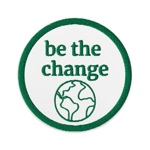 May include: Embroidered patch with a white center and a green border. The patch features the words "be the change" in green, along with a green outline of the Earth. The patch is circular.