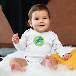 May include: A white long-sleeve baby onesie with a green circle graphic featuring a sea turtle and the text "Planet Over Plastic".