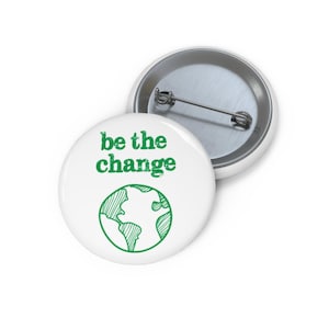 May include: A white ceramic mug with a black handle and the text "But First, Coffee" in a bold, black font. The mug is filled with a dark liquid, likely coffee, and sits on a light-colored surface.