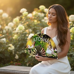 May include: A decorative fan with the name "LATOSHA" printed on it. The fan features a floral design with images of a person in a white dress. The fan is held in front of a background of white and yellow roses.