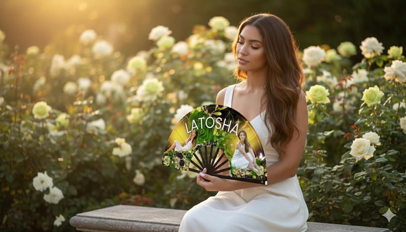May include: A decorative fan with the name "LATOSHA" printed on it. The fan features a floral design with images of a person in a white dress. The fan is held in front of a background of white and yellow roses.
