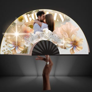 May include: A decorative fan featuring a photo of a couple embracing, with the names "Ethan & Jordyn" in elegant script. The fan is adorned with floral and glitter accents, and the word "BOOM" is visible at the top.