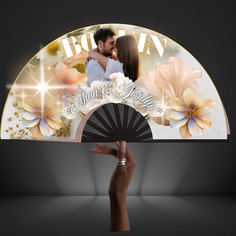 May include: A decorative fan featuring a photo of a couple embracing, with the names "Ethan & Jordyn" in elegant script. The fan is adorned with floral and glitter accents, and the word "BOOM" is visible at the top.