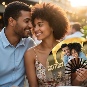 May include: A couple smiles, with the woman holding a personalized fan. The fan features a photo of the couple, the word "LOVE" in gold, and the names "ANTTONY" and "JESSICA". The fan has a black and brown design.