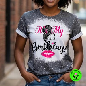 May include: A gray t-shirt with a white bleached design and rolled sleeves. The shirt features the text "It's My Birthday!" in pink and black, along with a graphic of a woman's face and pink lips.