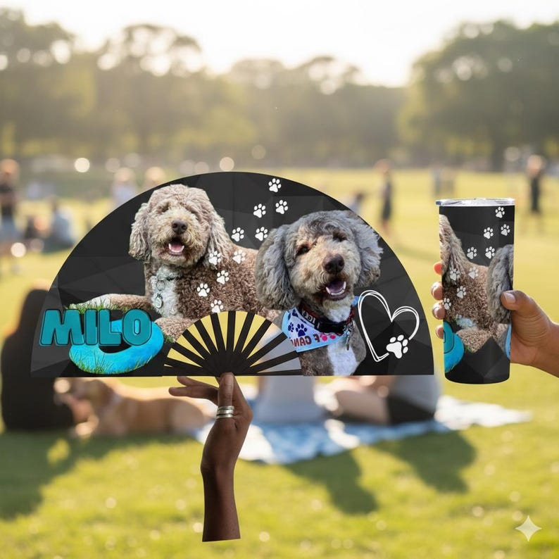 May include: A black fan and tumbler featuring two dogs with paw prints. The fan has the name "MILO" in blue and a heart with a paw print. The tumbler is held by a person.