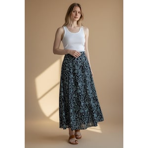 Op de afbeelding: Een wit geribbeld hemdje gecombineerd met een enkellange rok met hoge taille, voorzien van een donker marineblauwe basis en een lichtblauw bloemenpatroon. De rok heeft een ontspannen, vloeiend silhouet dat tot de enkels reikt, aangevuld met bruine sandalen.