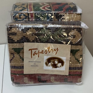 May include: Two folded tapestry bedding items packaged in clear plastic. The fabric features a multi-colored geometric and floral pattern in shades of tan, green, red, and blue. A label reads Tapestry Innovations in Bedding Portola Valley, California.